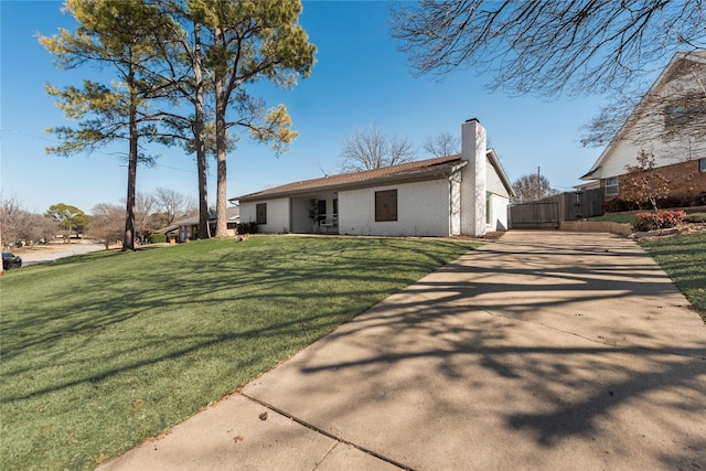 view of front facade with brick siding, a chimney, fence, driveway, and a front lawn