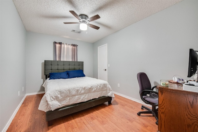 bedroom with a textured ceiling, wood finished floors, visible vents, and baseboards