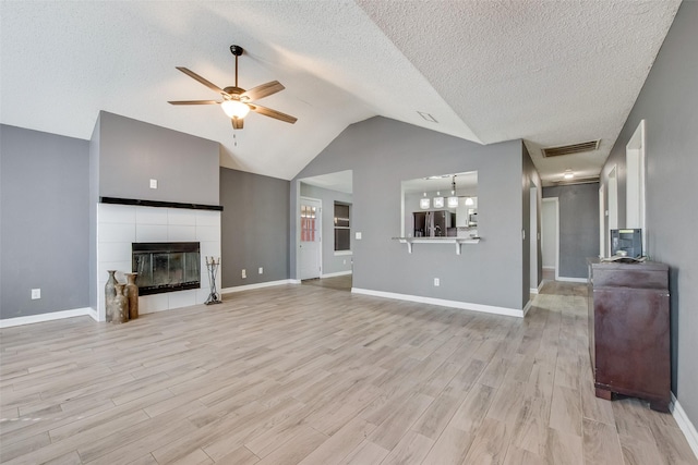 unfurnished living room featuring ceiling fan, a tile fireplace, visible vents, vaulted ceiling, and light wood-type flooring