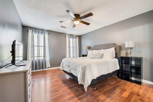 bedroom with a textured ceiling, wood finished floors, visible vents, and baseboards