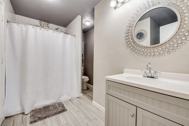 bathroom with a shower with shower curtain, toilet, vanity, wood finished floors, and baseboards