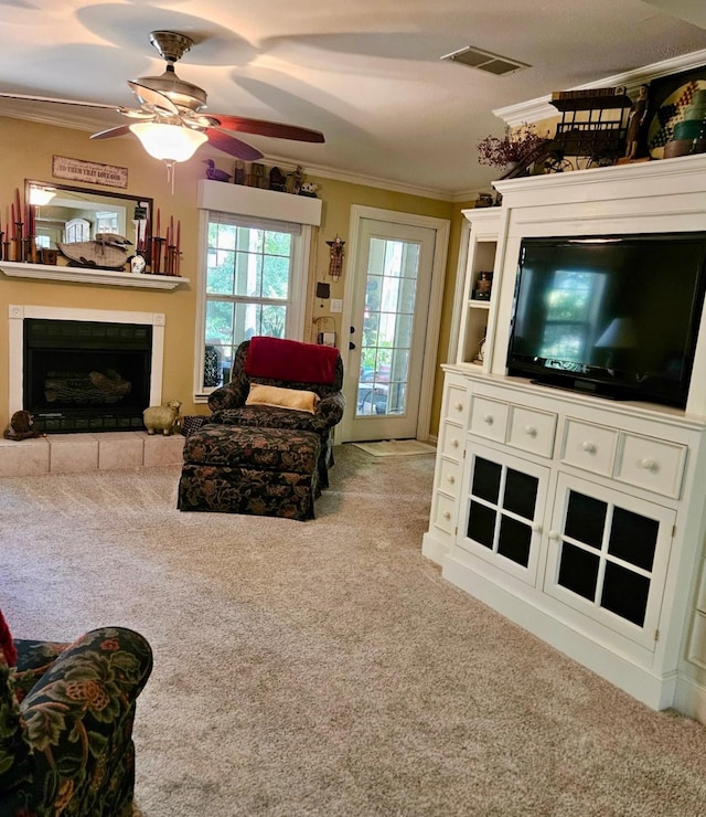 carpeted living room featuring a fireplace with raised hearth, ornamental molding, visible vents, and a ceiling fan