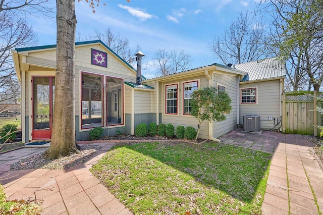 exterior space with a front lawn, fence, metal roof, and central AC