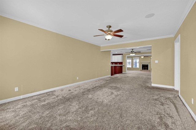 unfurnished living room with ceiling fan, a fireplace, baseboards, carpet, and crown molding