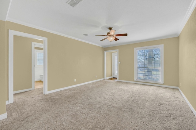 spare room featuring carpet floors, visible vents, ornamental molding, a ceiling fan, and baseboards