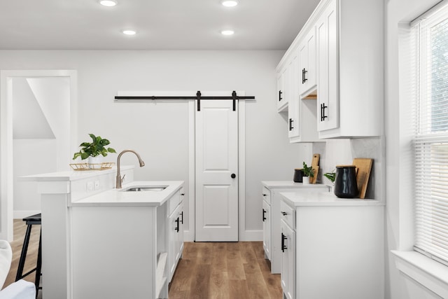 kitchen with a barn door, a breakfast bar area, a sink, white cabinetry, and light wood-type flooring