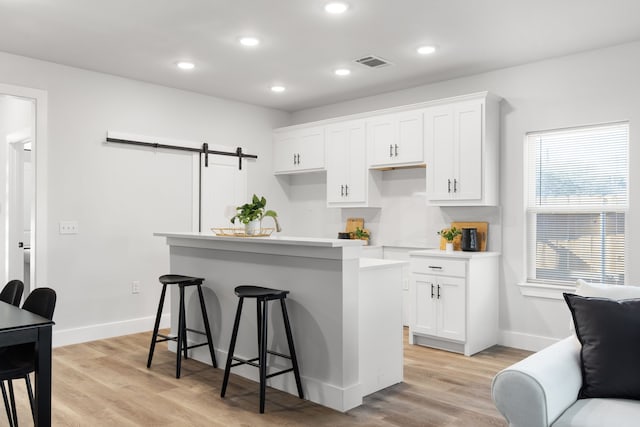 kitchen with a barn door, visible vents, white cabinets, a kitchen island, and a breakfast bar area