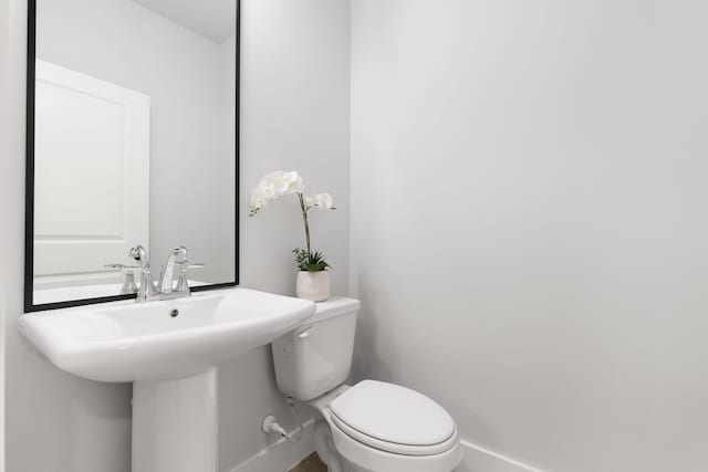 half bath featuring toilet, baseboards, and a sink