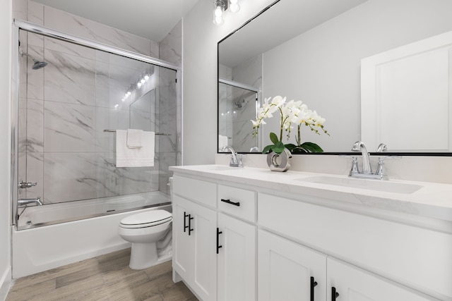 full bathroom featuring double vanity, toilet, combined bath / shower with glass door, a sink, and wood finished floors