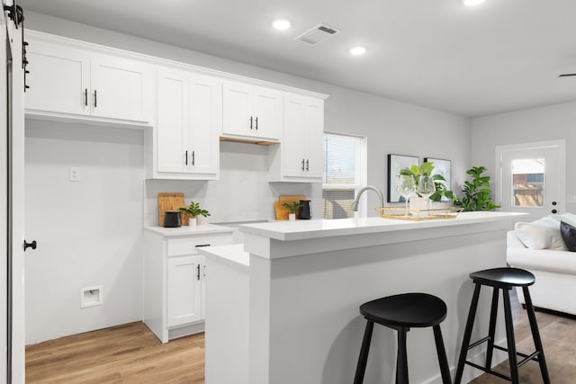 kitchen with light wood-type flooring, white cabinets, visible vents, and a healthy amount of sunlight