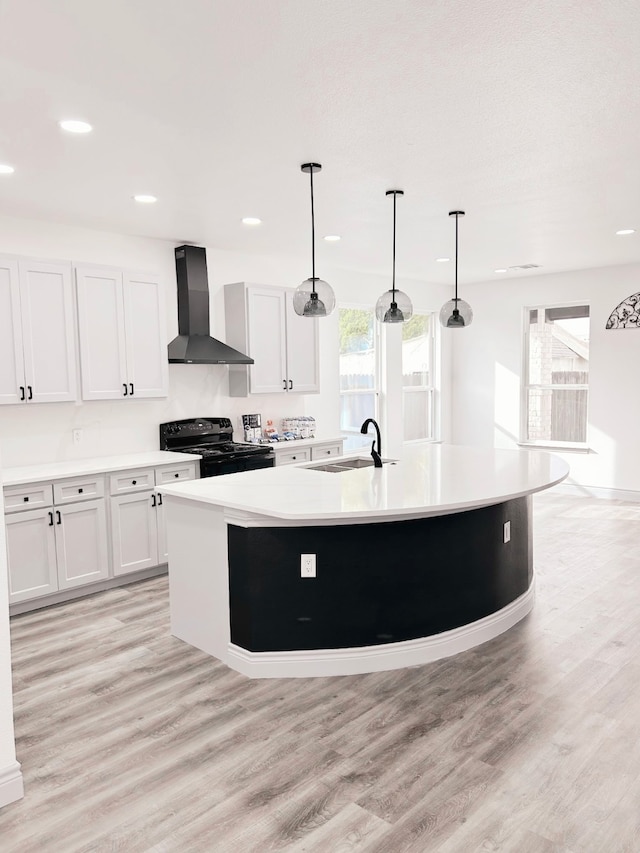 kitchen with wall chimney range hood, a center island with sink, light wood-style floors, black electric range, and a sink