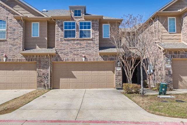 townhome / multi-family property with an attached garage, roof with shingles, concrete driveway, and brick siding