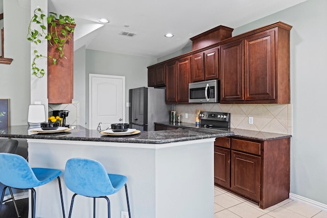 kitchen with visible vents, appliances with stainless steel finishes, a kitchen breakfast bar, a peninsula, and backsplash