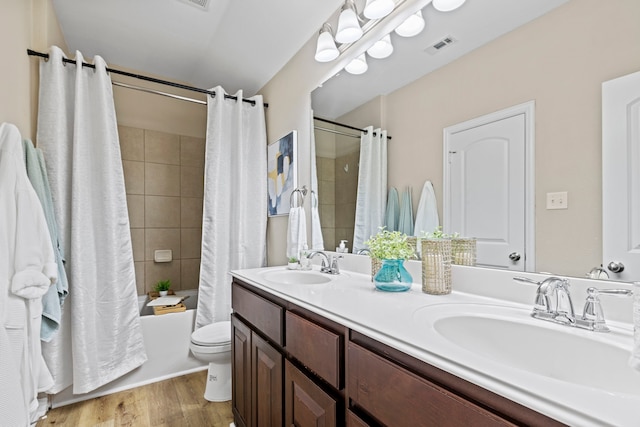 full bath featuring double vanity, wood finished floors, a sink, and toilet