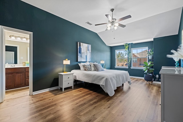 bedroom featuring lofted ceiling, ensuite bathroom, visible vents, baseboards, and light wood-type flooring