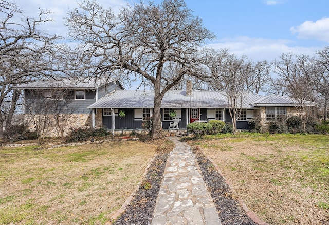 view of front of property featuring metal roof, a chimney, a front lawn, and a porch