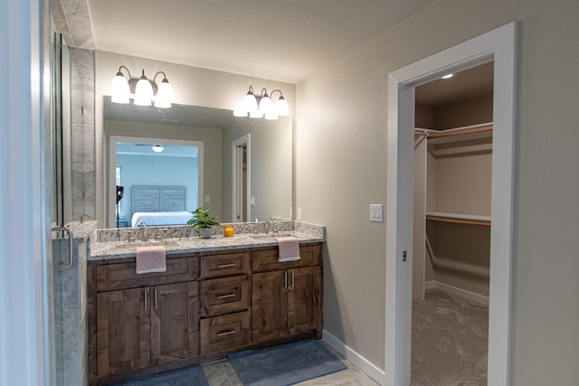 full bathroom featuring double vanity, baseboards, connected bathroom, a walk in closet, and a sink