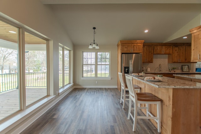 kitchen featuring wood finished floors, baseboards, vaulted ceiling, stainless steel fridge with ice dispenser, and tasteful backsplash