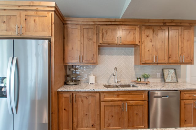 kitchen with light stone countertops, appliances with stainless steel finishes, backsplash, and a sink