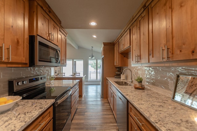 kitchen featuring lofted ceiling, appliances with stainless steel finishes, brown cabinetry, dark wood-type flooring, and a sink