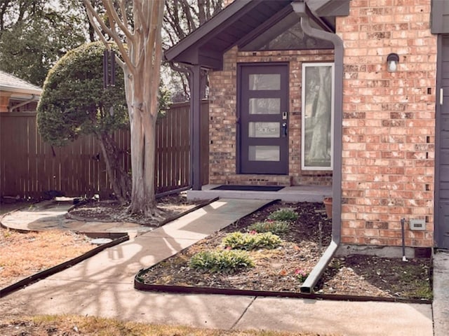 entrance to property featuring fence and brick siding