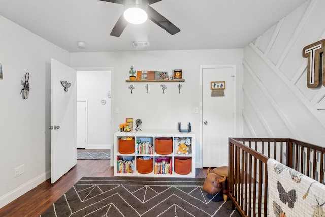 bedroom with ceiling fan, wood finished floors, visible vents, baseboards, and a crib