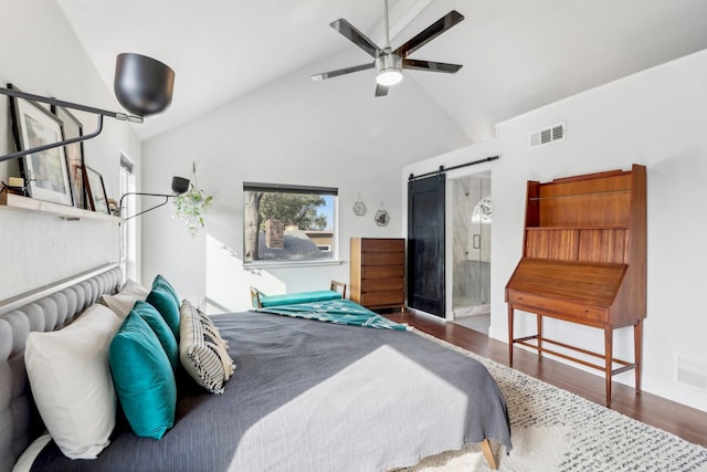 bedroom with lofted ceiling, a barn door, wood finished floors, and visible vents