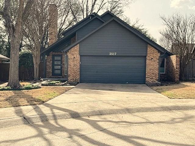 view of front of house featuring brick siding, fence, driveway, and an attached garage