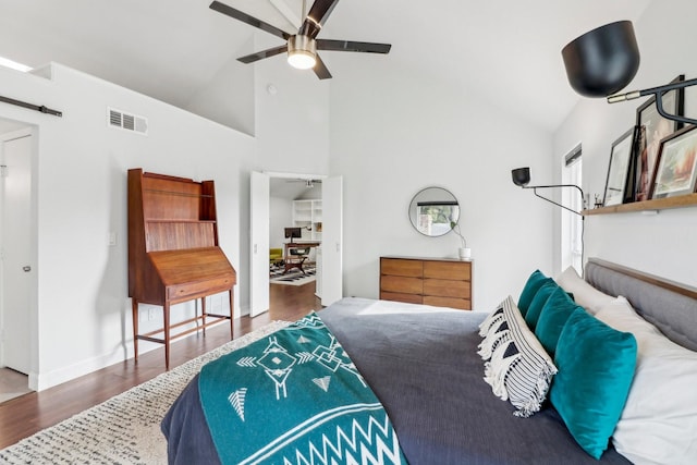 bedroom featuring visible vents, a barn door, wood finished floors, high vaulted ceiling, and baseboards