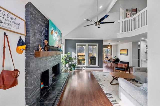 living area featuring a ceiling fan, a large fireplace, wood finished floors, high vaulted ceiling, and beamed ceiling