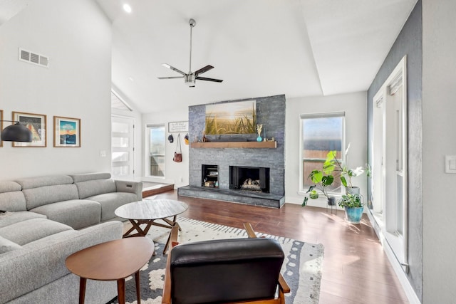 living room with high vaulted ceiling, a stone fireplace, wood finished floors, and visible vents