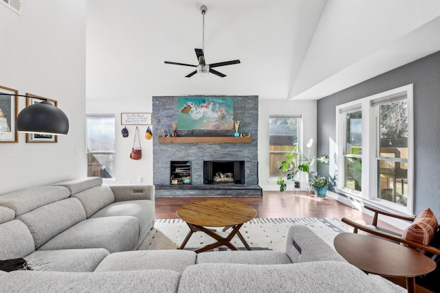 living area featuring high vaulted ceiling, visible vents, a stone fireplace, and wood finished floors