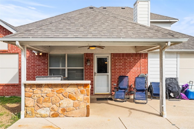 exterior space with a patio area, brick siding, roof with shingles, and a chimney