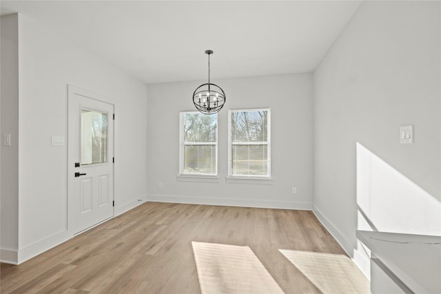 unfurnished dining area with an inviting chandelier, light wood-style flooring, and baseboards