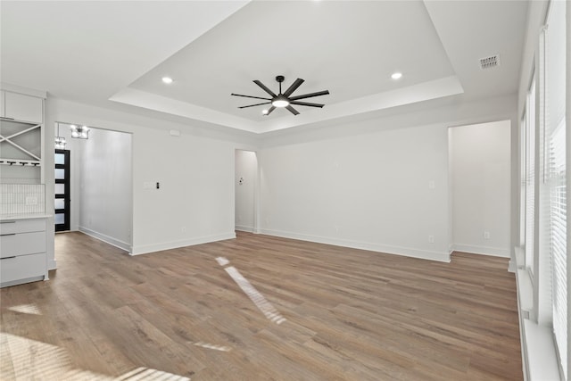 interior space featuring ceiling fan, light wood finished floors, a raised ceiling, and visible vents