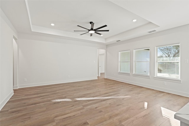 spare room featuring light wood-style floors, a tray ceiling, visible vents, and baseboards