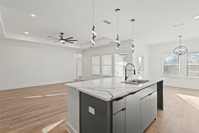 kitchen featuring a tray ceiling, decorative light fixtures, visible vents, light wood-style flooring, and a sink