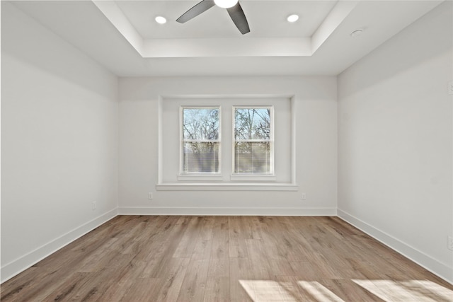 spare room with baseboards, a tray ceiling, and wood finished floors