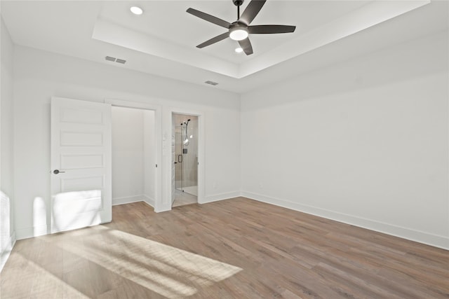 unfurnished bedroom featuring baseboards, visible vents, a raised ceiling, and wood finished floors