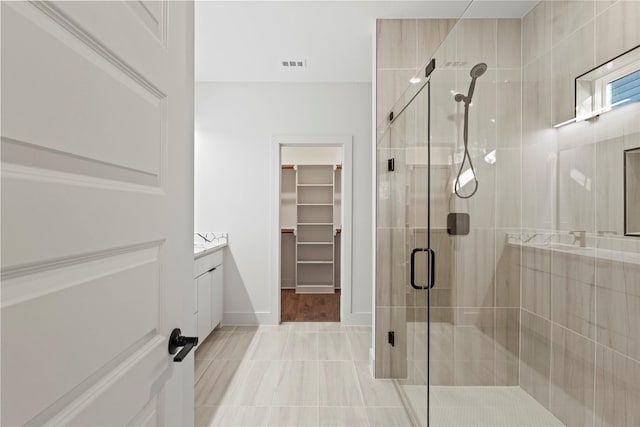 bathroom with a stall shower, baseboards, visible vents, a spacious closet, and vanity