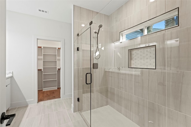 full bath with a stall shower, baseboards, visible vents, a walk in closet, and vanity