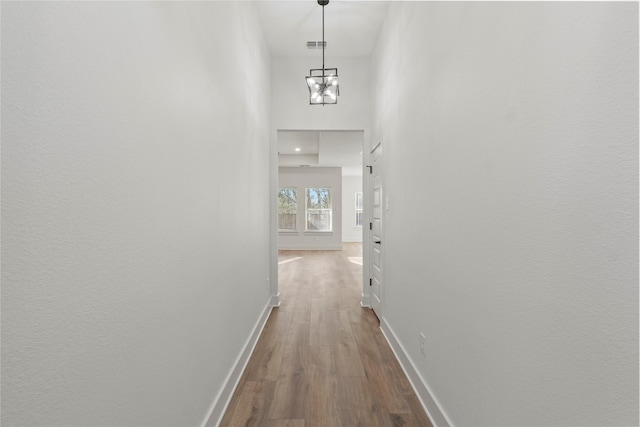 corridor featuring visible vents, a high ceiling, baseboards, and dark wood-style flooring