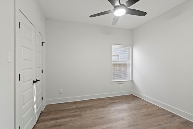 empty room with wood finished floors, a ceiling fan, and baseboards