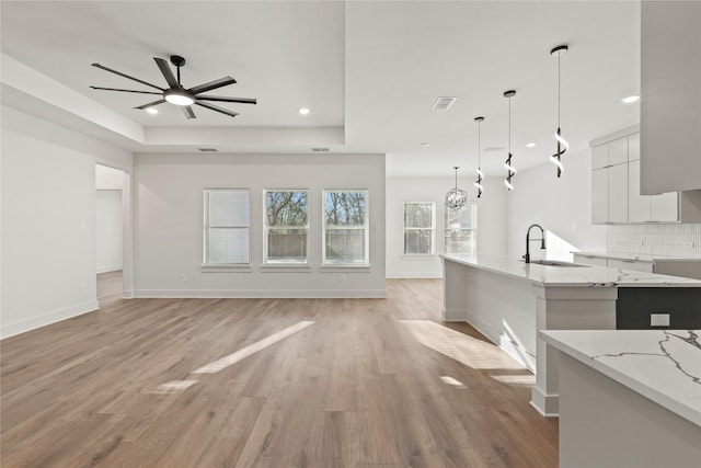 kitchen with decorative light fixtures, a raised ceiling, decorative backsplash, light wood-style floors, and modern cabinets