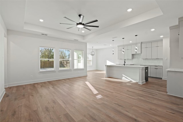 unfurnished living room featuring light wood-style flooring, visible vents, a raised ceiling, and ceiling fan with notable chandelier