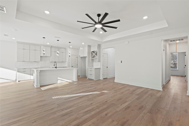 unfurnished living room with a ceiling fan, a raised ceiling, visible vents, and light wood-style flooring