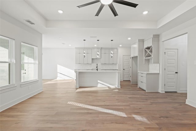 unfurnished living room with light wood-type flooring, visible vents, and a tray ceiling