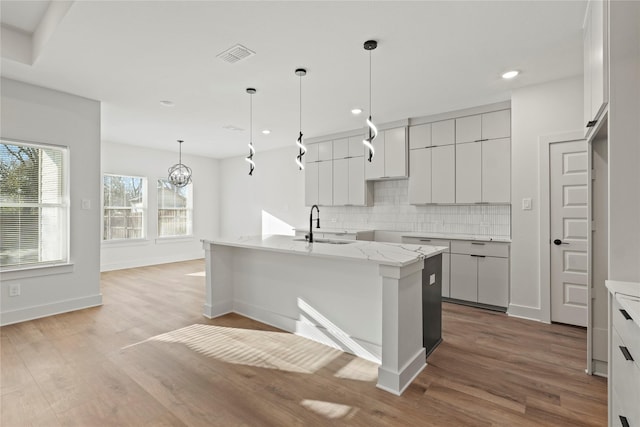 kitchen featuring tasteful backsplash, an island with sink, a sink, and light wood-style floors