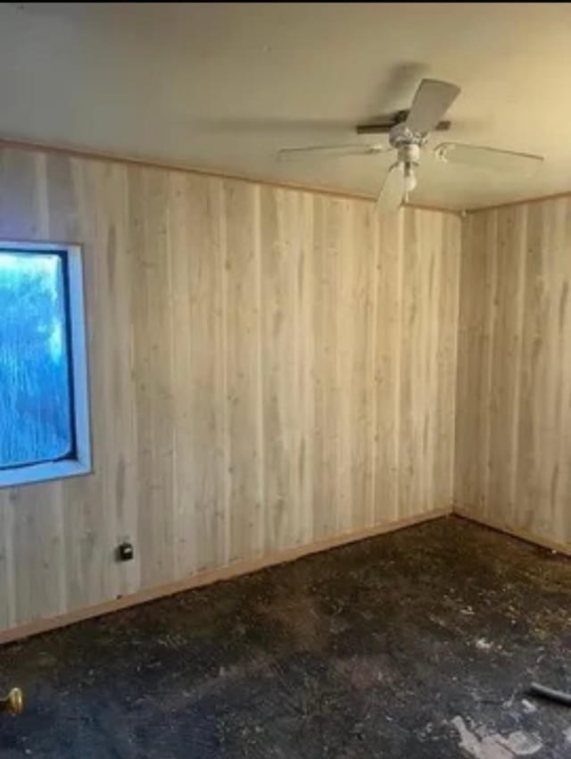 empty room with ceiling fan and wood walls