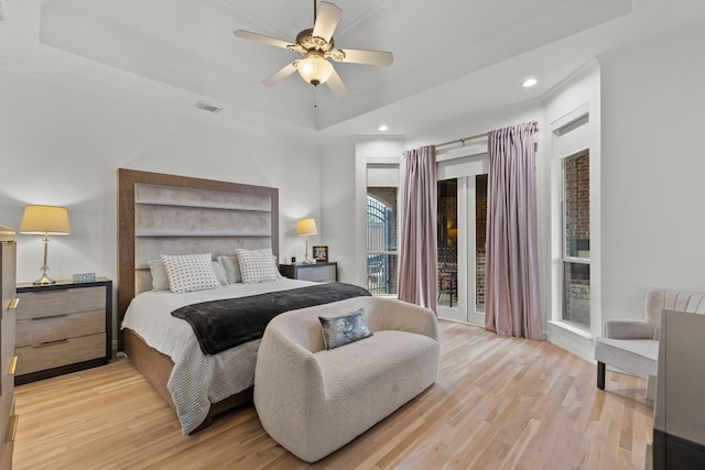 bedroom with a tray ceiling, crown molding, visible vents, light wood-style floors, and ceiling fan